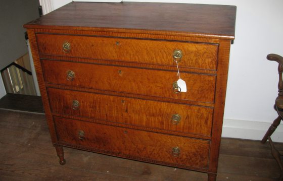 An antique maple dresser with a white tag hanging off a knob.