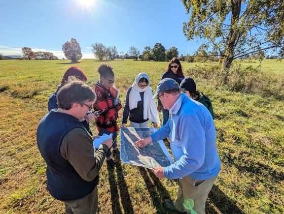 Six people standing outdoors in a circle looking at a map.