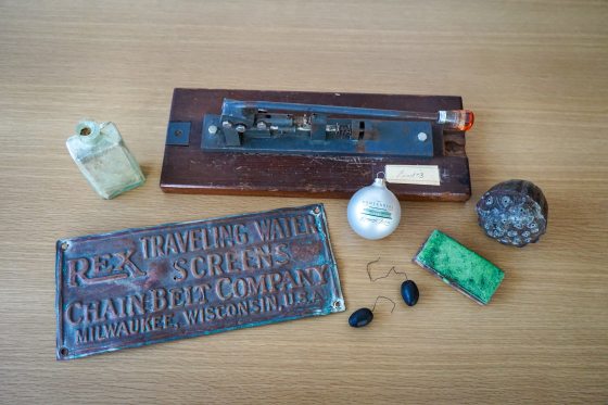 A variety of objects from the Longwood acchives featuring a glazed green tile, a Christmas tree ornament, and an 19th century hole puncher.