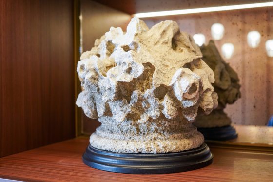 An old piece of stonework in an round shape with divots, displayed on a black stand.