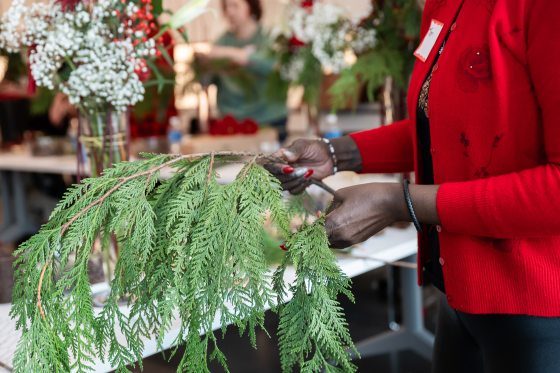 A person in a red jacket holding an evergreen branch intended for a floral arrangement.