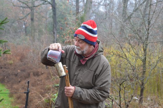 A person in a brown jacket and red and white stripped hat, filling a container with birdseed.