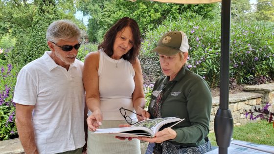 A person showing a book to two guests at Longwood Gardens.