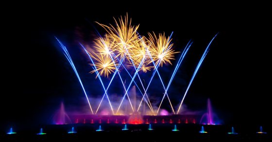 The Main Fountain Garden lit up at night with purple and yellow fireworks and an array of colorful fountains.