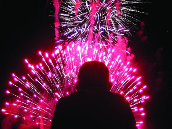 A silhouette of a person watching red fireworks explode in front of them.