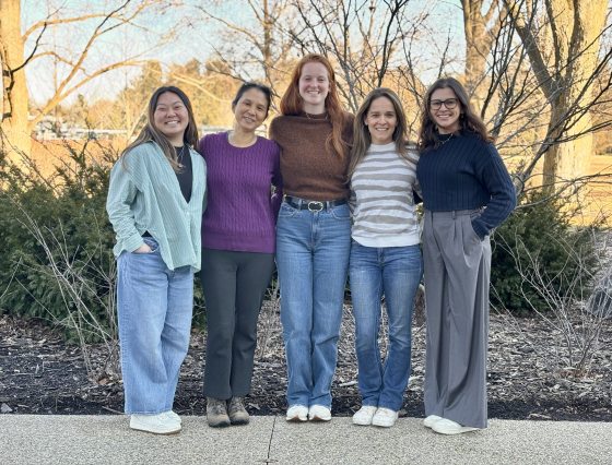 Five people taking a group photo, standing shoulder to shoulder, smiling at the camera.