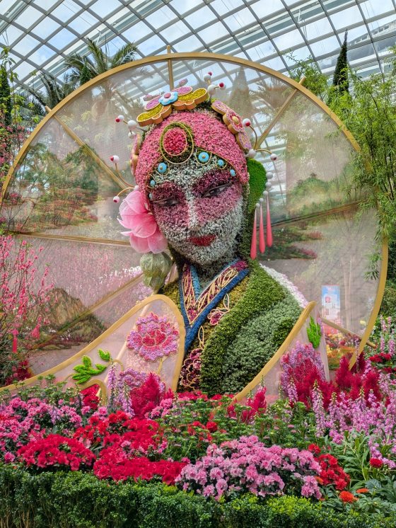 A sculpture of a female figure, made out of flowers, moss, and other natural materials.