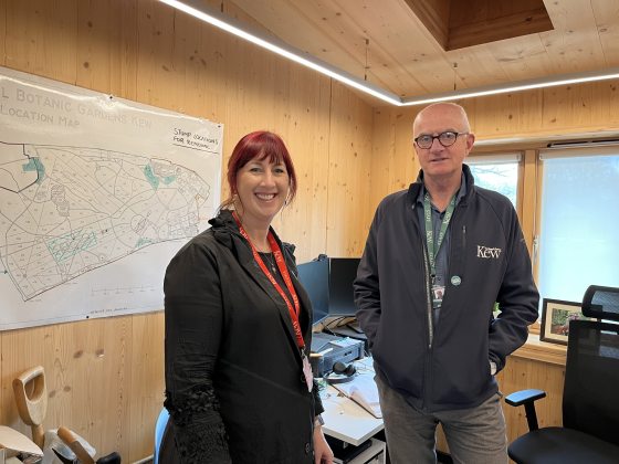 Two people standing inside a wood-paneled office, smiling at the camera.