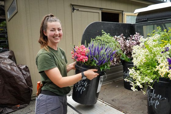 A person taking a bucket of cut flowers off the back of a cart and smiling at the camera.