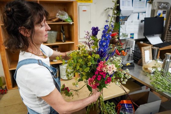 A person in a floral workshop arranging a pink and purple arrangement.