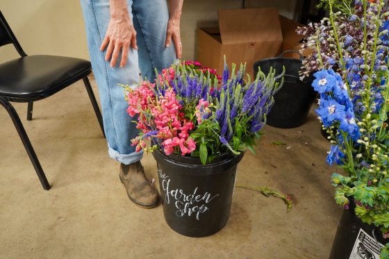 A black bucket of pink and purplr cut flowers in the middle of a floor.