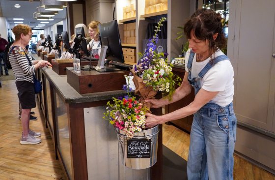 A person in denim overalls placing bouquets of flowers in a steel bucket.