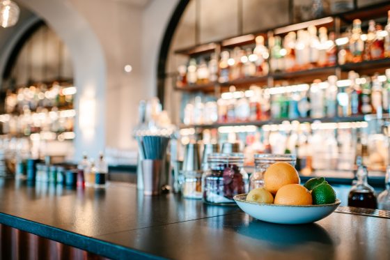 A bar countertop, with shelves of blurred liquor bottles behind it.
