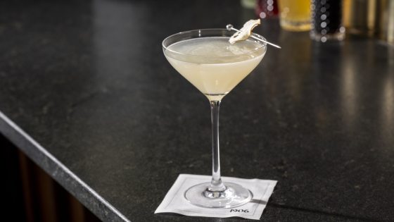 A white colored cocktail in a martini style glass on a black marble counter top.
