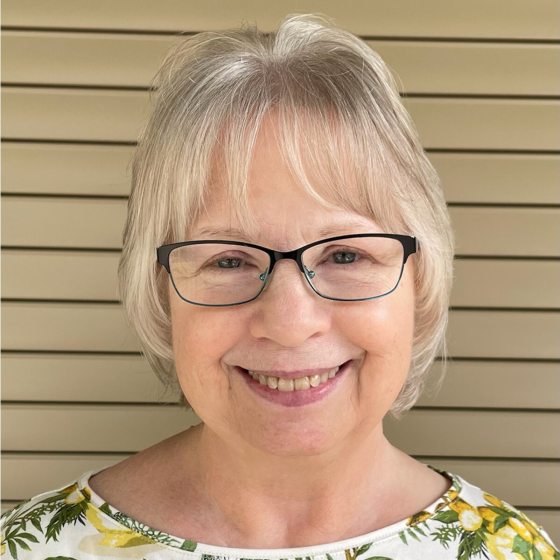 A headshot of a person with short blond hair, black glasses, smiling at the camera.