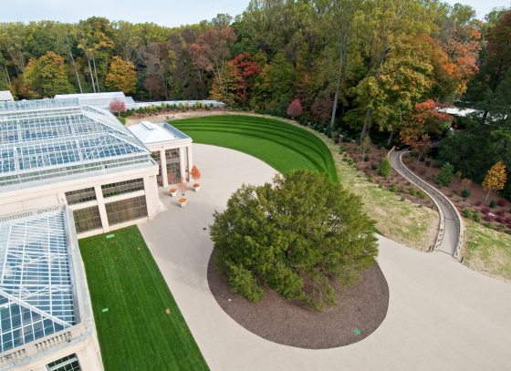 An aerial image of the East Conservatory Plaza, featuring a large English Yes in the center of a circular garden bed, and a portion of the glass conservatory.