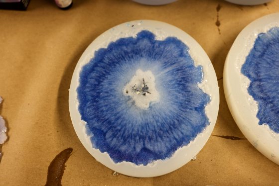 A close-up of a completed resin geode coaster in its white mold, featuring a deep blue, textured, crystalline center surrounding a small white core with silver glitter.