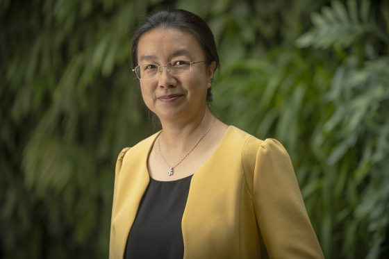 Close-up smiling headshot of a woman with glasses, a dark top, and a bright yellow blazer.