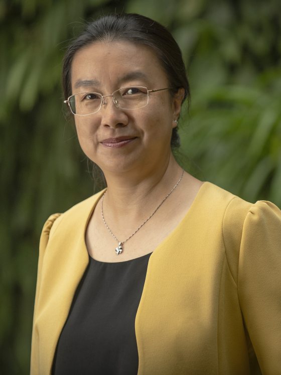 Close-up smiling headshot of a woman with glasses, a dark top, and a bright yellow blazer.