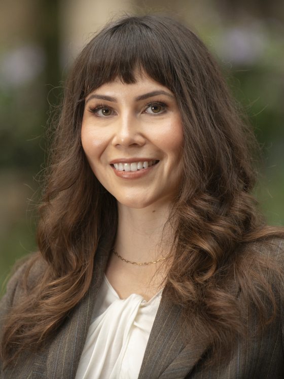 Close-up smiling headshot of a woman with dark hair, bangs, and a brown pinstripe blazer.