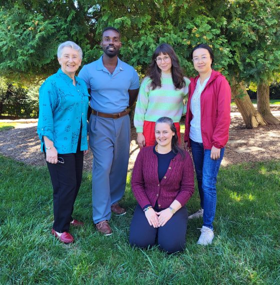 A group of five individuals, including President Susan Detwiler and four Longwood Fellows (Nathaniel Cody, Carmen Grey, Yan Li, Jennifer Dick), posing outdoors in front of a large evergreen tree.