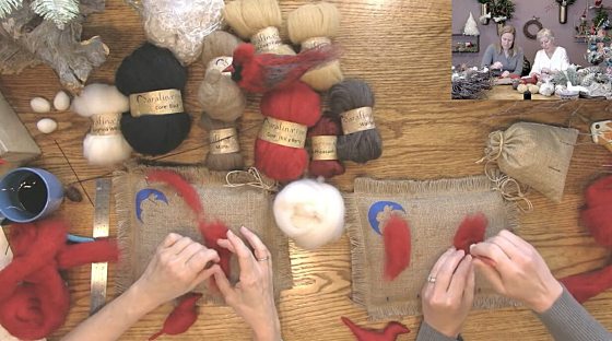 An overhead shot showing various colors of spun fiber/wool labeled "Sarafina" next to two pairs of hands crafting a red fiber bird shape on burlap mats. A small video inset in the corner shows two women working on a craft project.