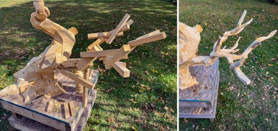 A rough, wooden model of a bonsai tree, made from stacked and carved MDF boards, sits on a wooden platform outdoors. Extra wooden blocks are glued to the side to form the armature for branches.