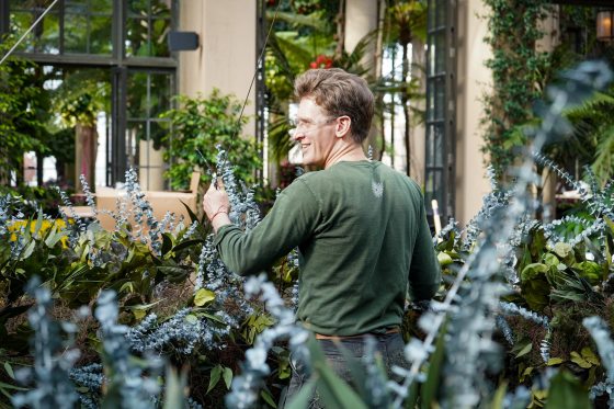 A staff member in a green shirt, looking to the left, installs a floral exhibit. 