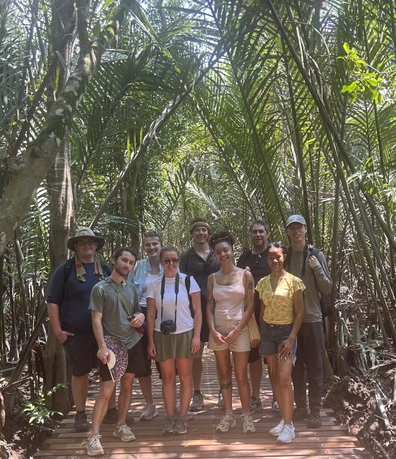 A group portrait of the Professional Horticulture class of 2026 standing on a wooden boardwalk inside a dense mangrove forest at Pulau Ubin, Singapore. The students are surrounded by tall, arching palm fronds and tropical trees.