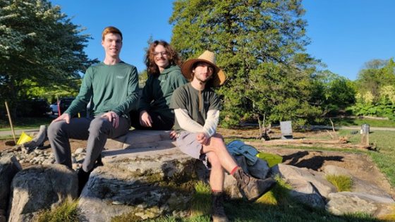 Three people sitting on a large rock, posing for the camera.