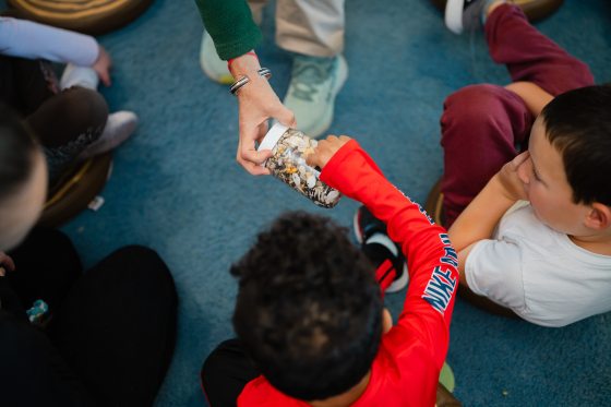An educator holds a clear plastic jar filled with various seeds for children to examine during an interactive educational workshop.