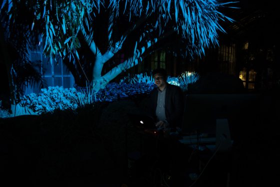 a person standing in an indoor garden with blue lights illuminated in the background