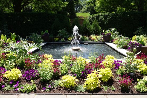 A square fountain surrounded by colorful summer plants
