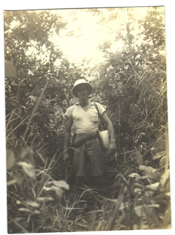 A woman stands among tall plants, dressed for an exploration